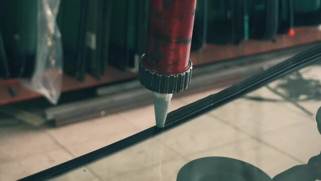 Process of preparing windshield for replacement in car service. Worker applies special adhesive sealant to windscreen before installation on auto.