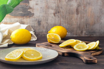 Cutting ripe lemons on a wooden cutting board and pieces on a plate on the table. Organic nutrition, source of vitamins.