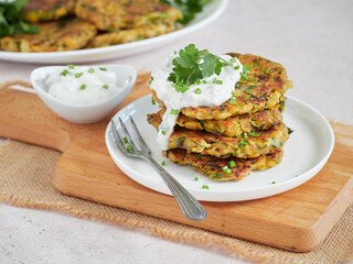 vegetable fritters, vegetarian pancakes, served in a pile on a white plate with sour cream and fresh herbs.