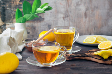 Two cups of tea with lemon, a sliced lemon and a bowl of honey on a wooden table. Vitamin warming drink