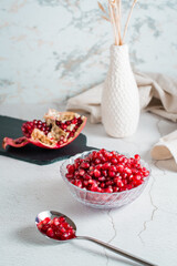 Grains of a ripe pomegranate in a bowl and in a spoon and a part of a pomegranate on a light table. Organic natural food. Vertical view