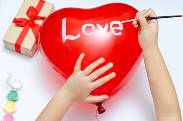 A 5-year-old girl gives her mother balloons with inscriptions mom and love and boxes with a gift for the holiday. Blurry, defocused, selective focus.