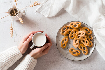 Bavarian pretzels on a plate and a cup of milk in female hands on the table. Snack for fast food. Top view.