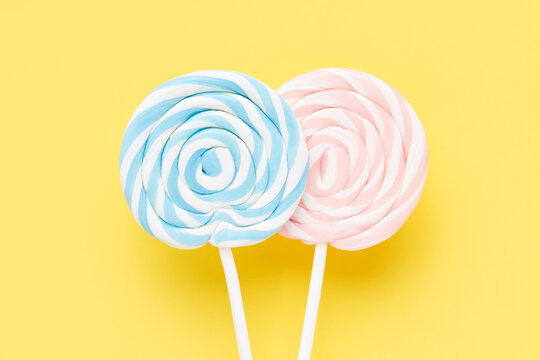 Two colorful lollipops on a white stick on a yellow background. Top view, copy space