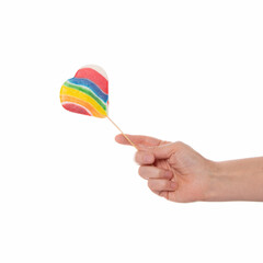The hand holds a lollipop in the shape of a heart and rainbow colors on a white background. A symbol for love, Valentine's Day, the gay community.