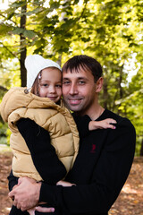 Fototapeta premium Dad and daughter are hugging and looking at the camera. Summer park. Green trees. The concept of a young family.