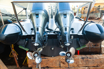 Two outboard motors at the stern of a motorboat resting on wooden blocks in dry dock.