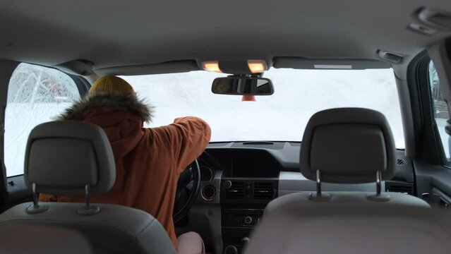 Young man trying to scraping a frozen car windshield in cold winter