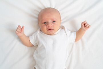 a newborn baby cries on a white sheet. childish tantrums. top view.