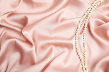 Beautiful pearls on pink silk, top view. Space for text