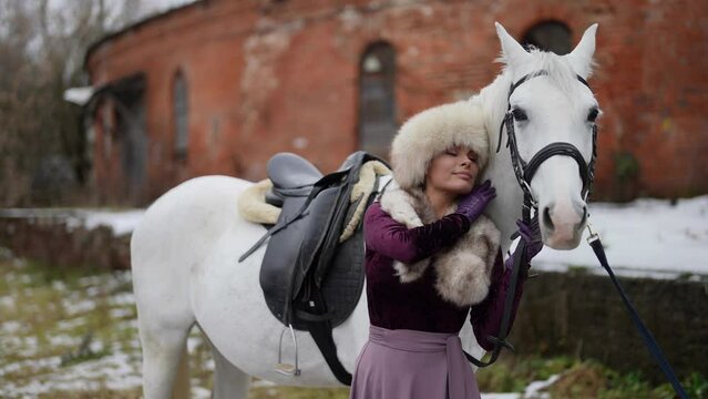 beautiful woman and white horse in yard in winter day, historical and fairytale concept