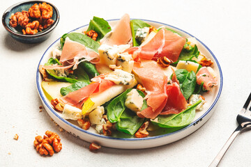 Summer pear salad with jamon, blue cheese, spinach and nuts on white table background, top view, copy space