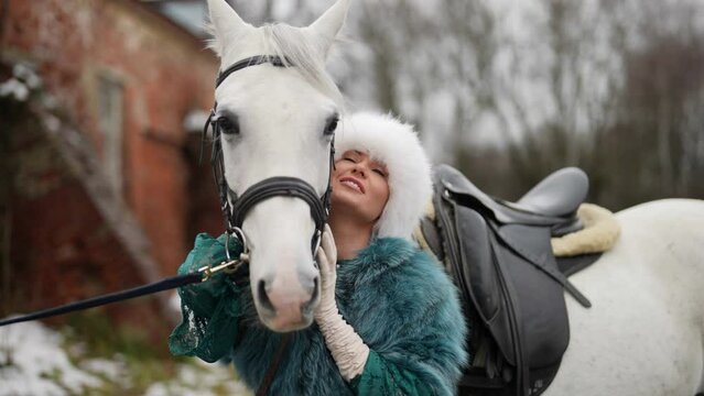 beautiful woman is embracing white stallion tenderly in horse yard