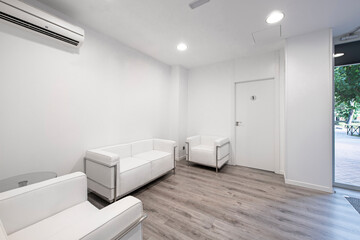 Waiting room in a clinic with air conditioning, white walls and sofas and gray wooden floors