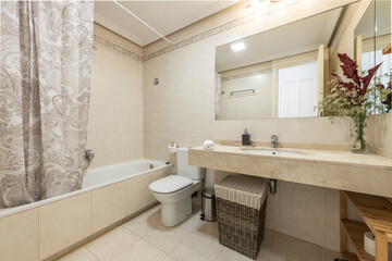 Bathroom with cream marble countertop, long bathtub with curtain, bouquet of dried flowers, porcelain sink and built-in mirror in vacation rental apartment