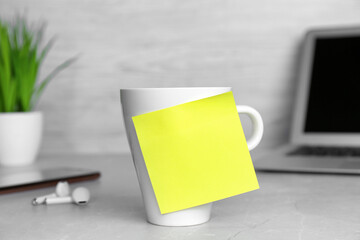 Cup with blank sticky note on white office table. Space for text