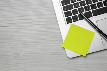 Laptop with blank sticky note and pen on white wooden table, top view. Space for text
