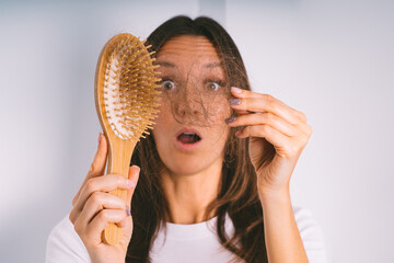 Young woman shocked because of hair loss problem. Woman holding hair brush and showing damaged...