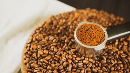 Ground coffee in portafilter on wooden board with coffee beans. Freshly ground coffee in filter holder and roasted beans for preparation of fragrant drink.