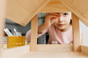 Caucasian girl kid colors wooden bird feeder, winter bird care and children's creativity at home....