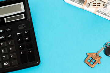 Buying a home. Keys with a keychain in the form of a house, money and a calculator on a blue background with a place for the text. real estate for sale