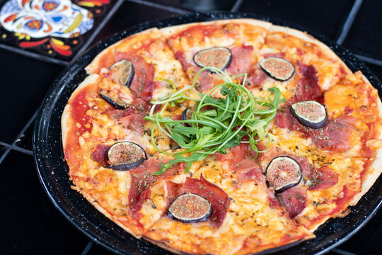 Pizza de jamón serrano con higos y arúgula sobre mesa negra 