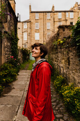 Fototapeta na wymiar Young female posing with a red raincoat in the middle of a close during a rainy summer day in Edinburgh.