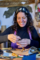 Fototapeta premium Smiling craftswoman working leather at the work table in her studio