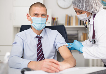 Doctor in face mask uses hypodermic needle and a syringe to put a shot of drug to patient in hospital office