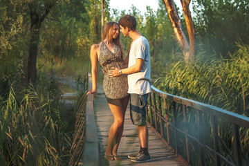 A beautiful couple in nature stands hugging on a wooden bridge over a river overgrown with reeds. Happy lovers celebrate Valentine's Day together.