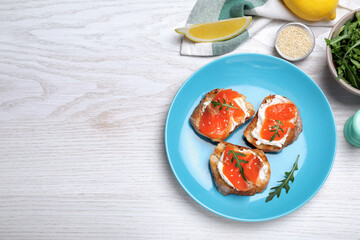 Delicious sandwiches with cream cheese, salmon and arugula served on white wooden table, flat lay. Space for text
