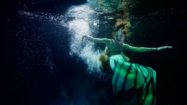 mysterious mermaid is swimming in dark depth of sea or lake, woman with fake fishtail