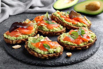 Delicious sandwiches with salmon, avocado and herbs on grey table, closeup