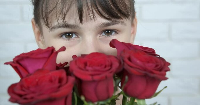 Trendy teen with flowers. A nice happy teenager girl hide her face in red roses in the hoom.