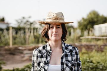 Young farmer woman looking at camera with greenhouse on background - Focus on face
