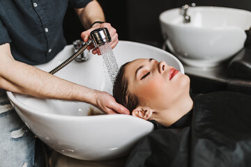 Professional hairdresser washing hair of a beautiful young adult woman in hair salon.