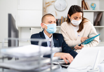 Businessman in protecrive mask talking to female colleague in office