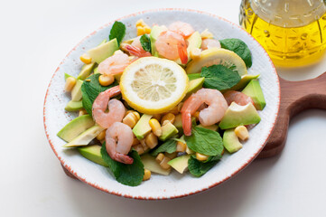 Salad with shrimp, avocado, corn and lemon with olive oil on a white background. Salad with shrimp and avocado on wooden background with oil olive bottle