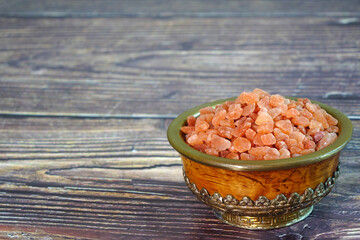 Pink Himalayan salt in Antique Tibetan bowl on wooden table. Selective focus with copy space