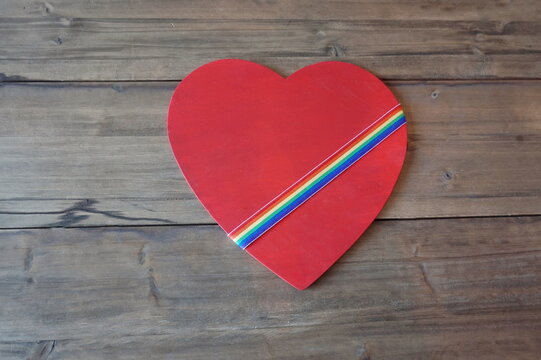 Wood Heart Cutout Painted Red with Rainbow Ribbon Diagonal on Dark Wooden Panels