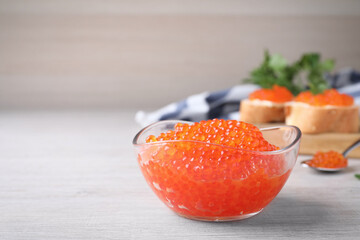 Glass bowl with delicious red caviar on white wooden table. Space for text
