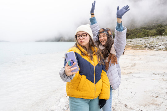 Two teen gesturing funny while taking a selfie in front of a alpine lagoon