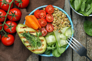 Delicious lentil bowl with avocado, tomatoes, carrot and cucumber on wooden table, flat lay