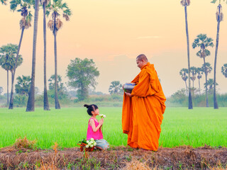 Buddhist monk going about with alms bowl to receive food and girl giving food to monk in morning in...