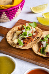 Traditional Mexican street food called "Tacos al pastor" prepared with pork, tortillas, pineapple, cilantro, onion, green sauce, red sauce and lemons. On white texture background.