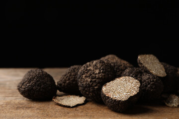Whole and cut truffles on wooden table against black background, closeup