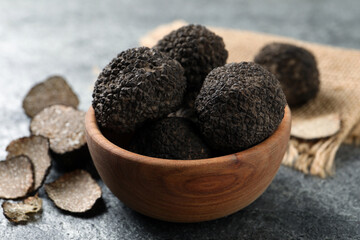 Black truffles with wooden bowl on grey table, closeup