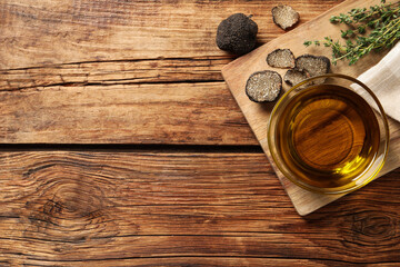 Fresh truffles, thyme and oil in glass bowl on wooden table, flat lay. Space for text