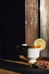 white teacup with gold greek key on windowsill with lemon wheel garnish and tiny rosebuds