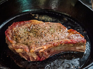 Close up shot of frying aged ribeye steak in a cast iron pan